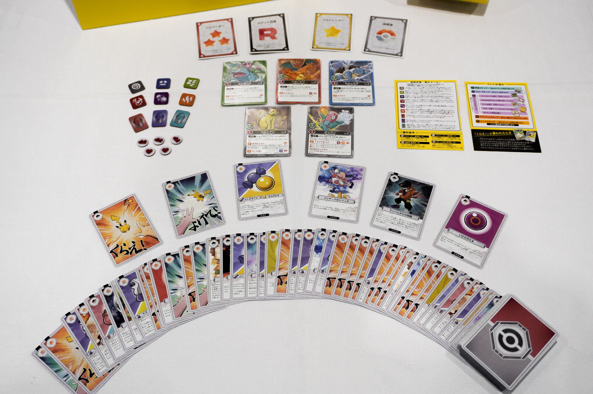 Full component spread showing the four role cards, Venusaur, Charizard, Blastoise, Persian and Porygon Pokémon cards, damage markers, reference sheets and a fan of play cards